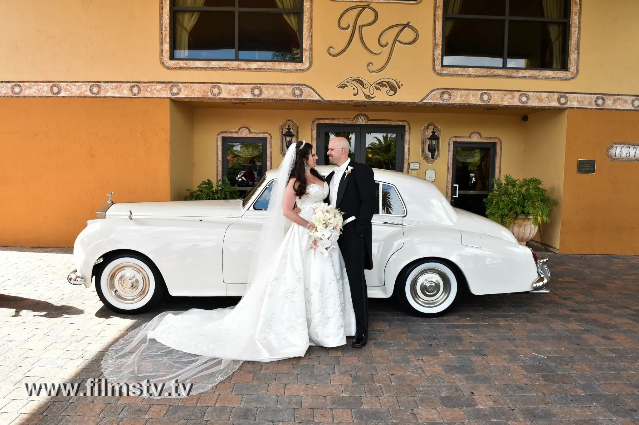 A bride and groom posing in front of a classic car.